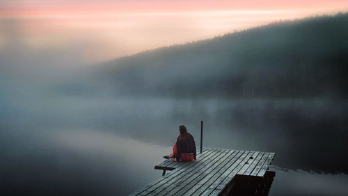 Girl sitting on pier against sky