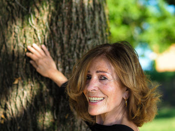 Portrait of a smiling young woman against tree trunk