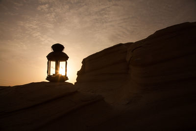 Silhouette rock on sand against sky during sunset