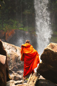 Rear view of man standing on rock against waterfall