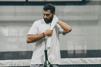 Beautiful man playing padel tennis racket in hand wipes the sweat. young sporty boy after the match