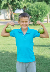 Funny boy with green apples shows biceps. vertical shot.