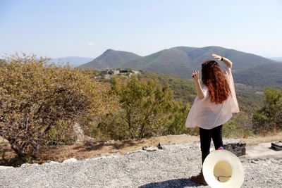 Rear view of woman with arms raised against clear sky