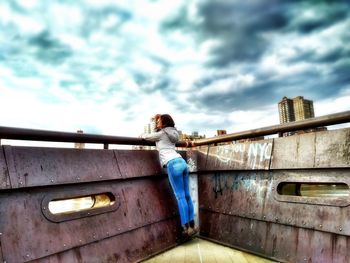 Man standing on bridge against cloudy sky