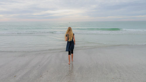 Rear view of woman standing on beach against sky