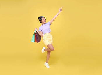 Full length of woman jumping against yellow background