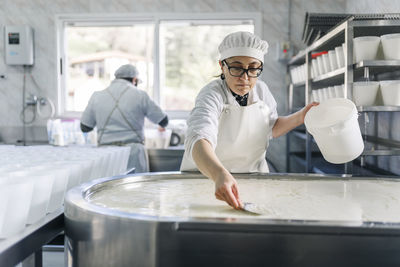 Female chef making cheese with colleague in background at factory
