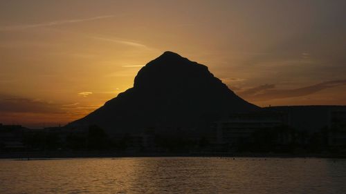 Silhouette mountain by sea against orange sky