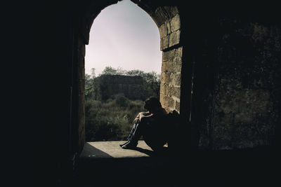 Depressed man sitting at arch window of historic building