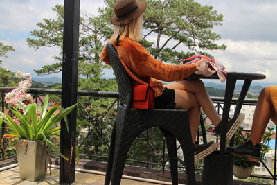 Woman sitting on chair by plants against sky