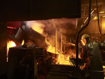 Rear view of worker working by furnace in foundry