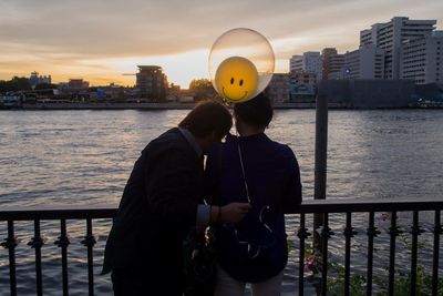 Person standing by river against sky during sunset