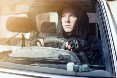 Man wearing hood driving car seen through windshield