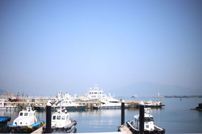 Boats moored at harbor against clear blue sky