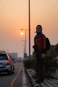 Portrait of smiling woman standing by road against sky during sunset