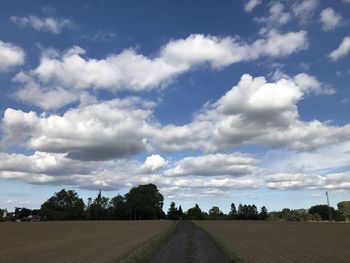 Road by trees on field against sky