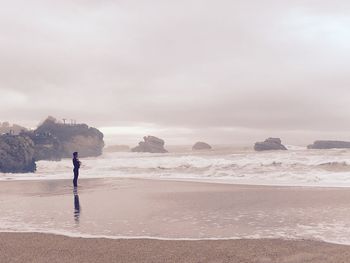 Man standing at sea shore against cloudy sky