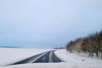 Road amidst snow covered landscape against clear sky