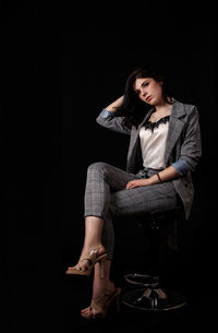 Young woman looking away while sitting on chair against black background