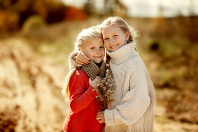 Two sisters in warm sweaters hug and run along the trail in the autumn forest. happy children