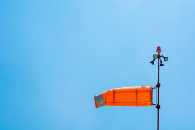 Low angle view of orange windsock waving against clear blue sky