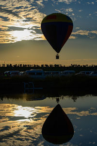 Hot air balloon flying over lake against sky during sunset