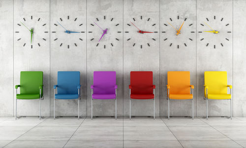 Colorful empty chairs arranged against wall with clocks