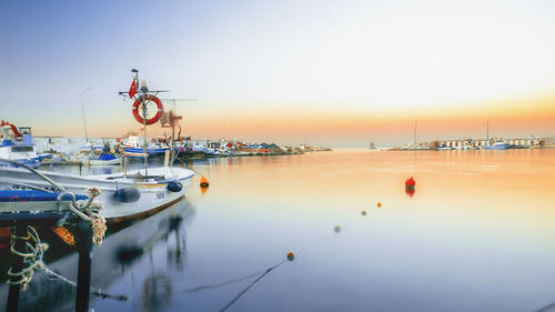 Sailboats moored in harbor against sky during sunset