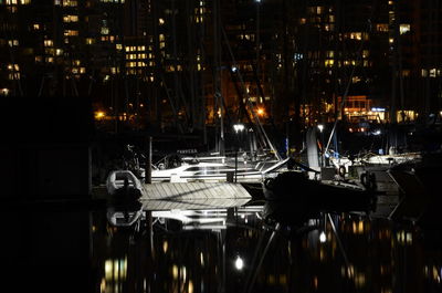 Sailboats moored in illuminated city at night