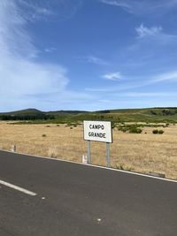Information sign on road by field against sky