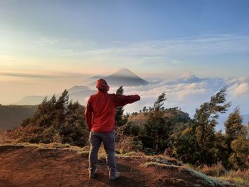 Rear view of man standing on mountain against sky