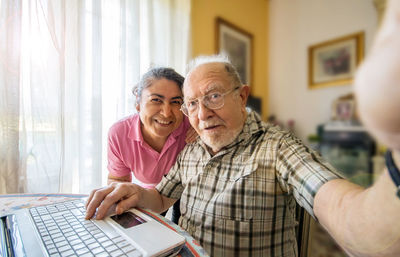 Portrait of smiling senior man with nurse doing selfie at home