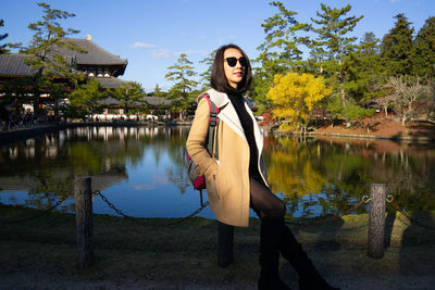 Portrait of young woman standing by lake against trees