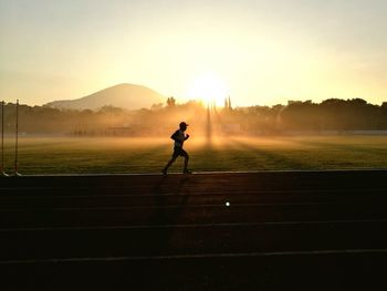 Man running on sports track against sky during sunset