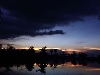 Silhouette trees by lake against sky at sunset