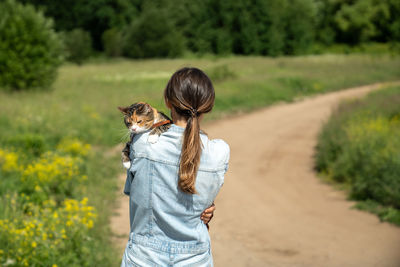 Rear view of woman hugging calm peaceful cat tightly while walking in rural countryside nature area