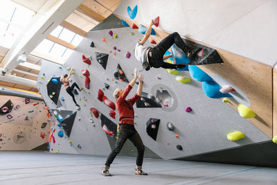 Male trainer training man in wall climbing at gym