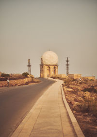 Rear view of man walking on street against clear sky with radar tower in background