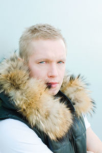 Portrait of man wearing fur jacket against blue wall