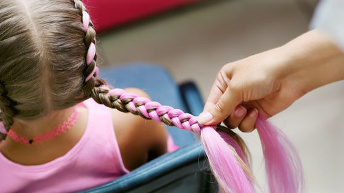 Beautiful blond girl, of seven years old, braided two pigtails, do a hairstyle with pink locks of