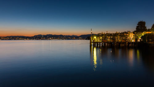 Illuminated buildings by sea against sky at night