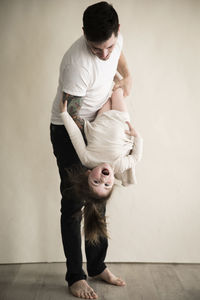 Happy tattooed millennial dad holds toddler daughter upside down