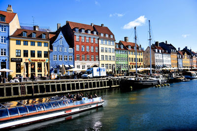 Boats moored in canal by buildings against sky