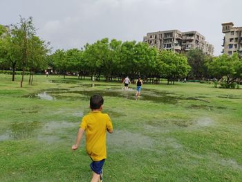 Rear view of children playing on grassland against trees
