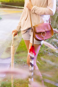 Midsection of woman carrying umbrellas and purse at park