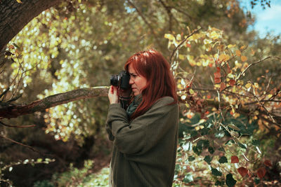 Young woman photographing with camera while standing in forest