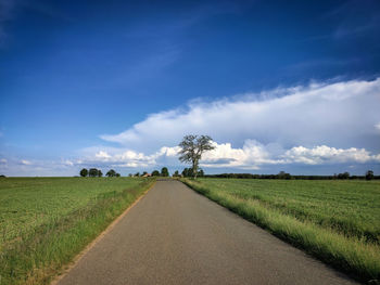 Empty road amidst field against sky