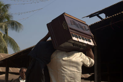 Rear view of man carrying harmonium