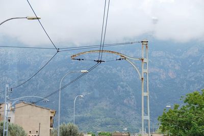 Electricity pylon by street against sky