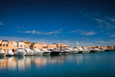 Boats in sea by buildings against blue sky